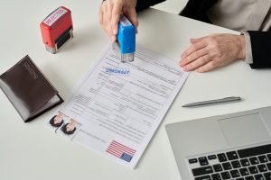 Oficial de inmigración sellando un formulario de solicitud de visa en una oficina de USCIS, ilustrando la nueva tarifa biométrica 9-11 para H-1B y L-1
