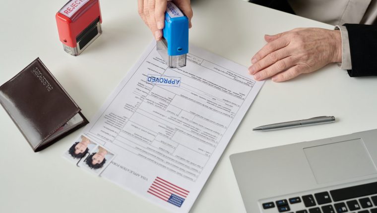 Oficial de inmigración sellando un formulario de solicitud de visa en una oficina de USCIS, ilustrando la nueva tarifa biométrica 9-11 para H-1B y L-1